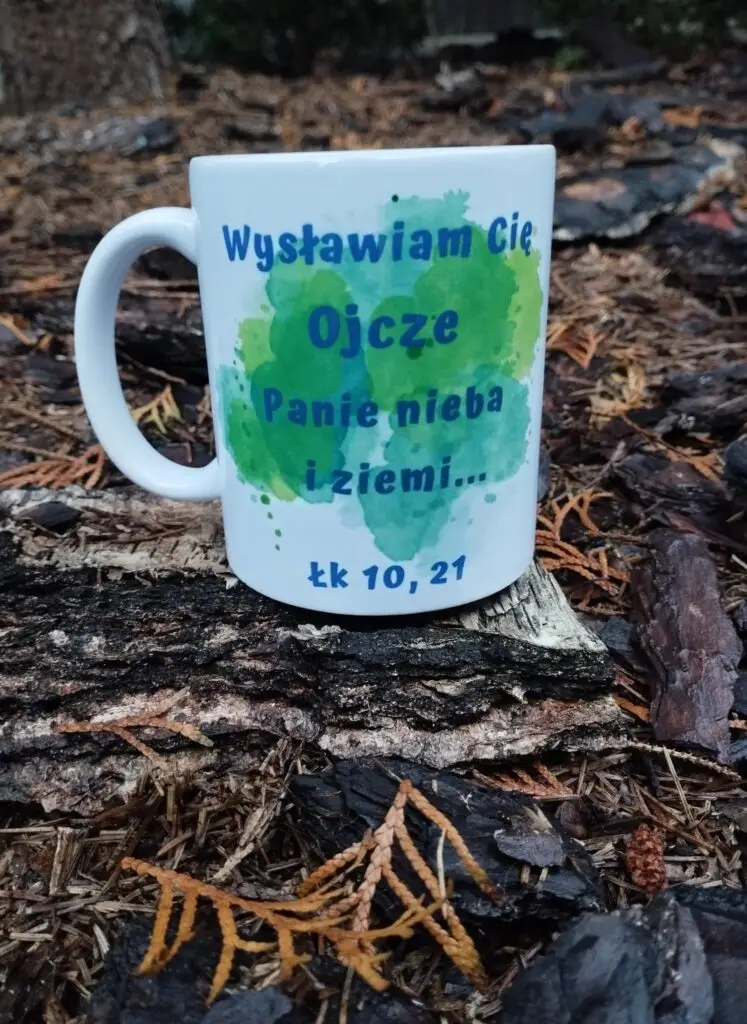 Biały kubek chrześcijański Wysławiam Cię Ojcze Panie nieba i ziemi na akwarelowym tle ustawiony na korze drzewa
