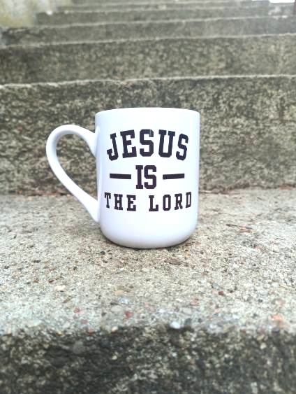 Biały kubek z ciemnym napisem „Jesus is the Lord” na kamiennych schodach